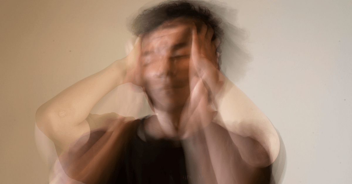 A blurred, double-exposed image of a man holding his head with both hands, conveying a sense of emotional distress, confusion, or anxiety