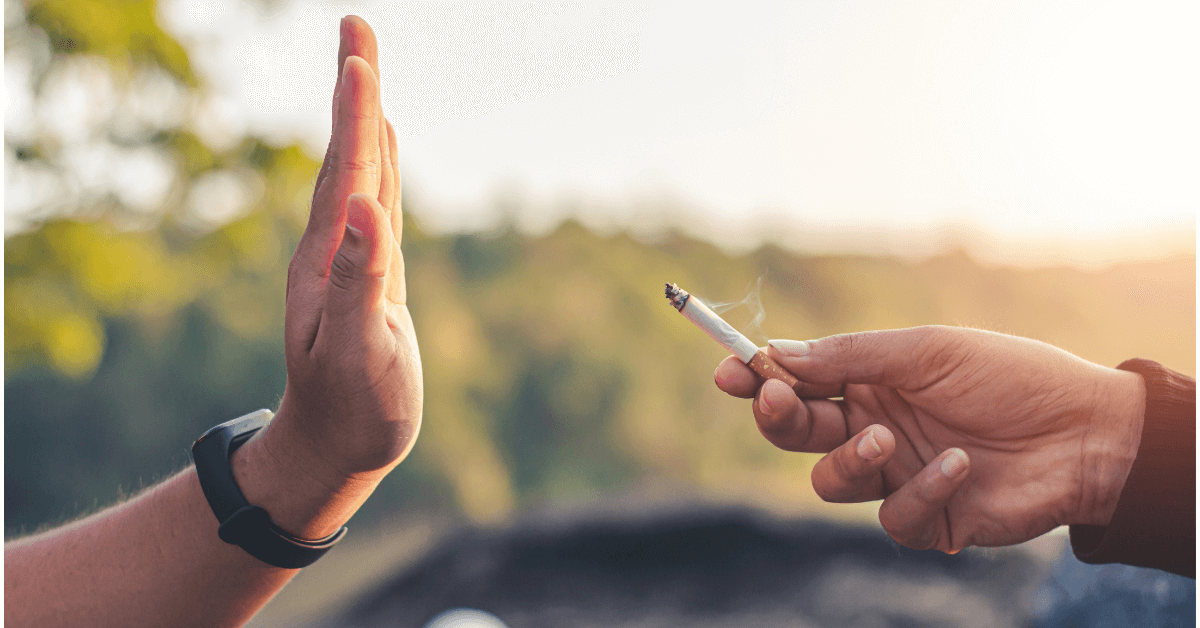 A person extends a lit cigarette towards another individual, who responds by raising their hand in a "stop" gesture.